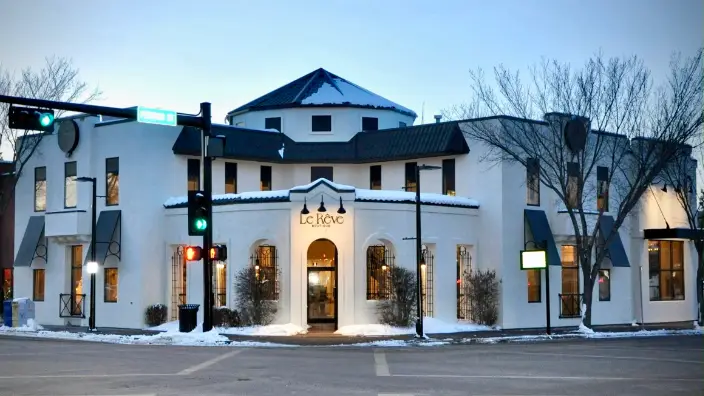 The Bruin Inn located in St. Albert, a two-story building with a white façade and curved architectural details, illuminated by exterior lights against a twilight sky, with snow on the ground indicating winter season.