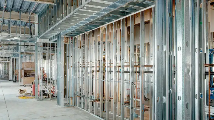 Interior view of a commercial building under construction, featuring metal stud framing, exposed utilities, and unfinished concrete flooring.