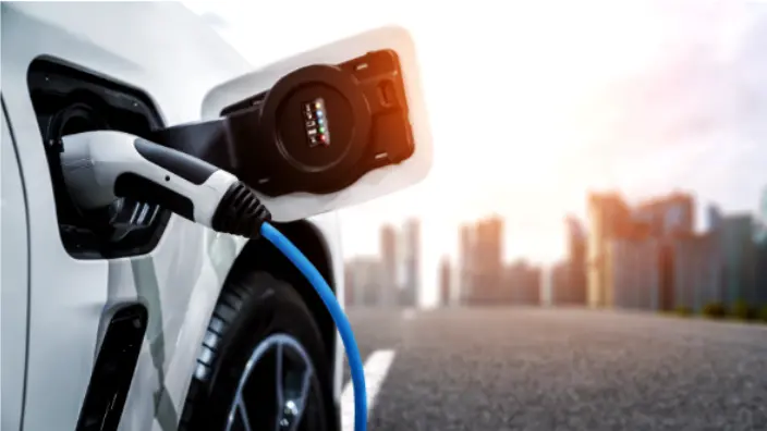 Close-up of an electric vehicle's charging port with a plugged-in cable, set against a blurred city skyline background, highlighting the concept of sustainable transportation and modern urban living.