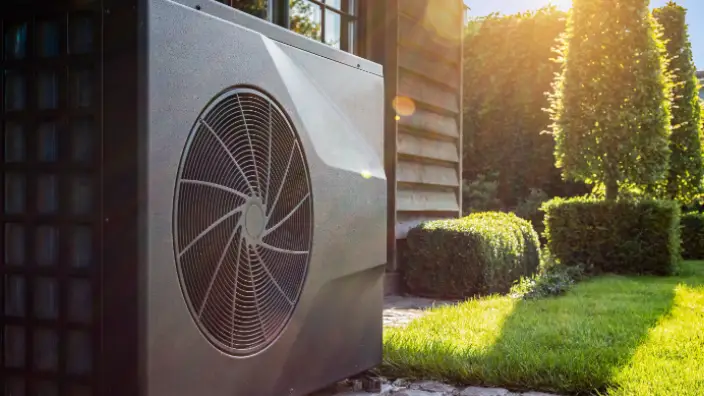 A heat pump system outside a house, with sunlight casting a glow on the unit and the surrounding greenery, indicating an eco-friendly heating and cooling solution in a residential setting.